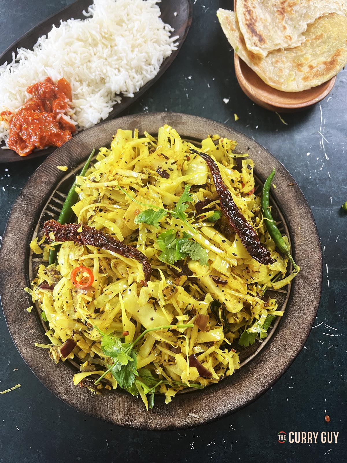 Cabbage thoran in a serving dish with rice and parathas.