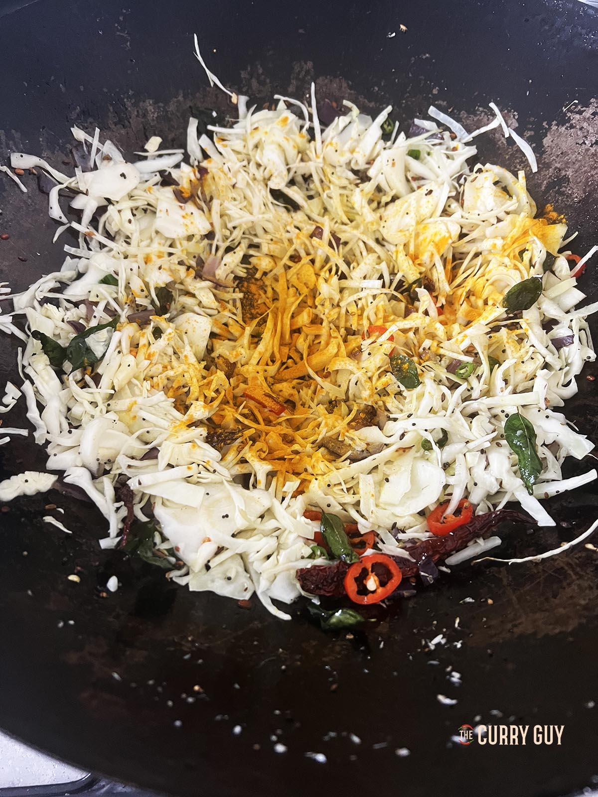 Adding the cabbage and ground spices to the wok.