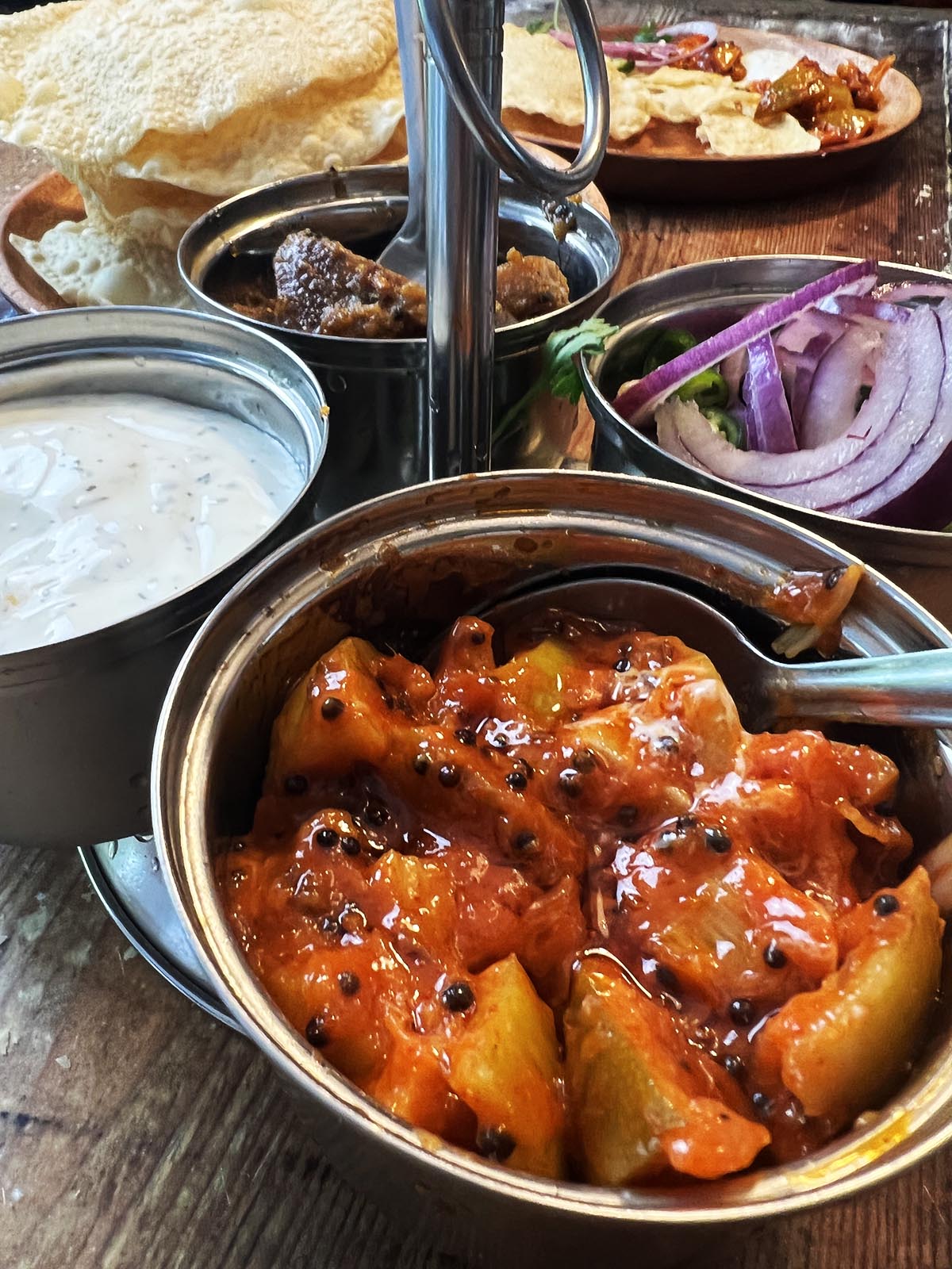 Lime pickle being served with other raitas and pickles and poppadoms