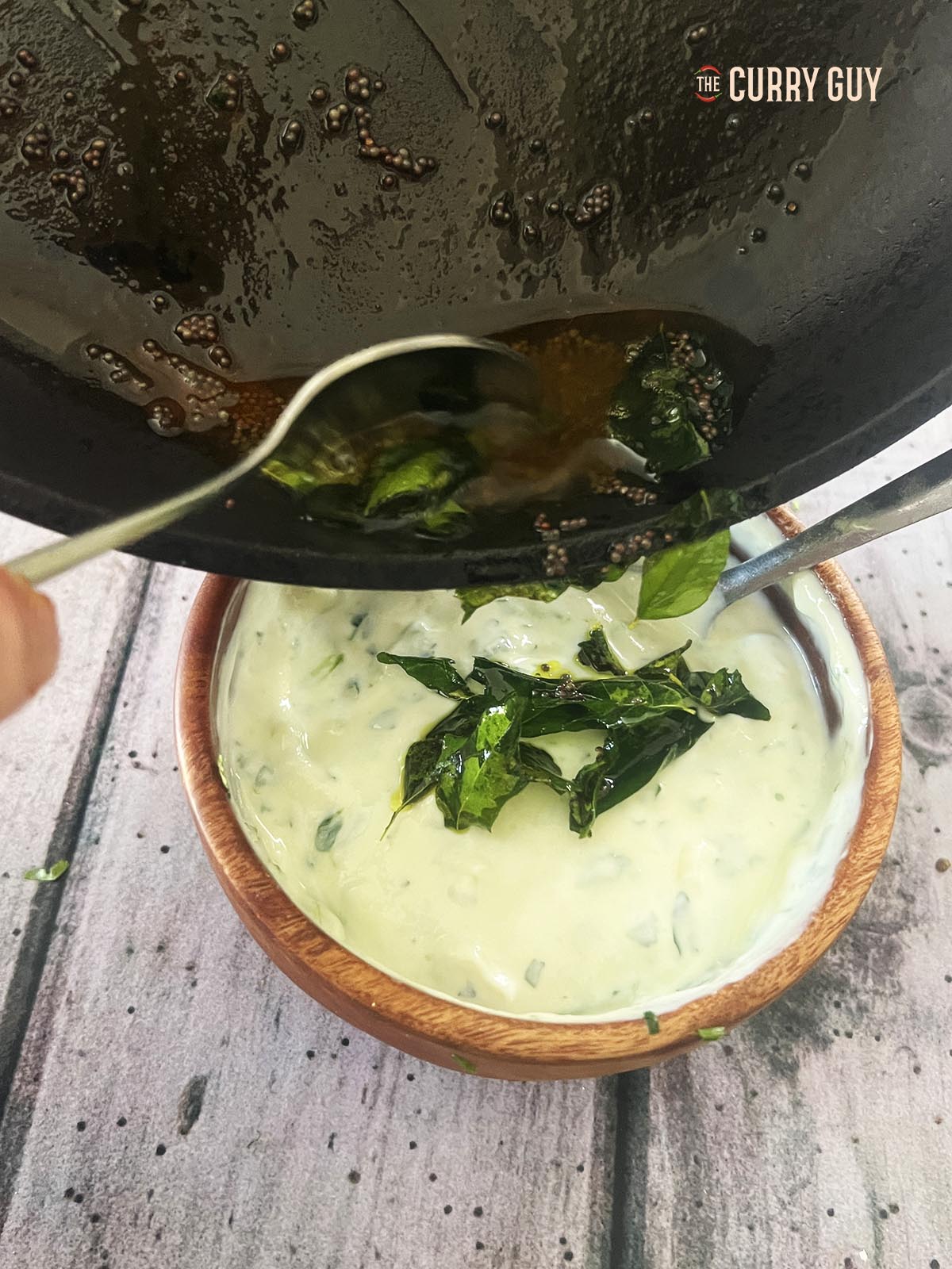 Pouring the cooled infused oil over the raita.