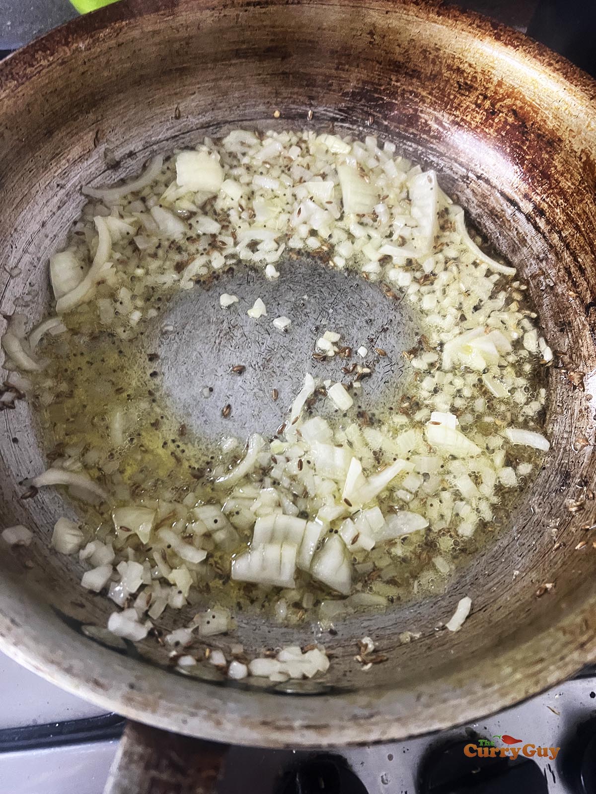 Adding onions to the pan to fry until soft and translucent.