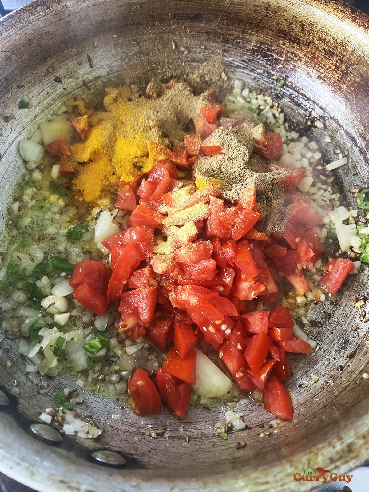 Stirring ground spices and chopped tomatoes into the other ingredients.