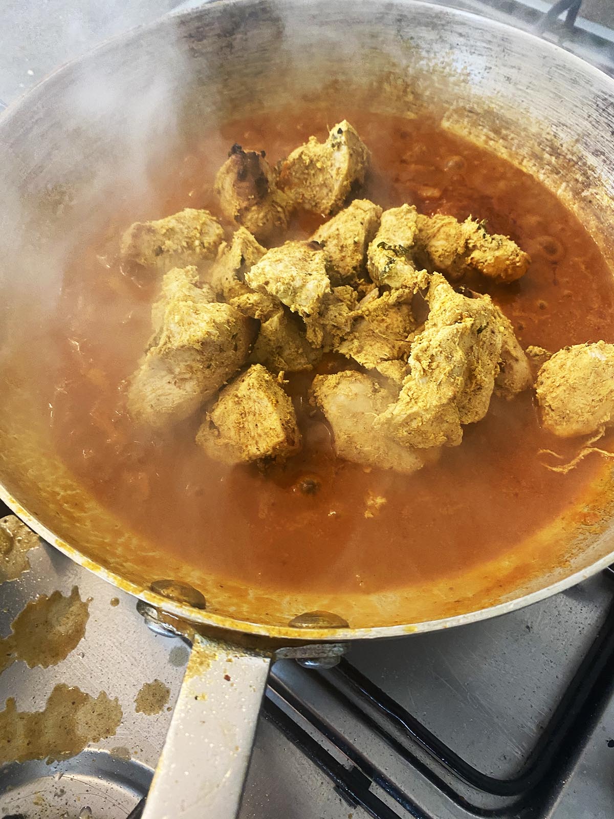 adding pre-cooked chicken to the curry sauce in the pan