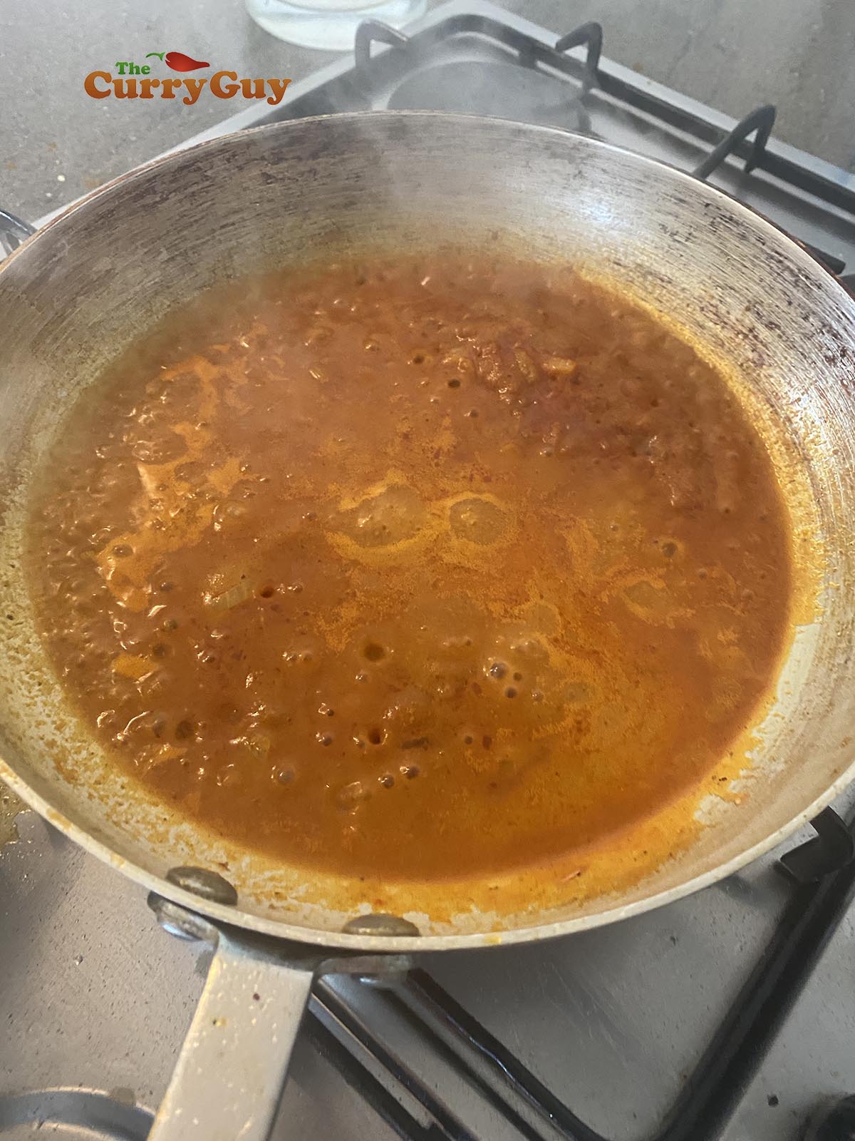 Adding base sauce to the pan and bringing it to a simmer.