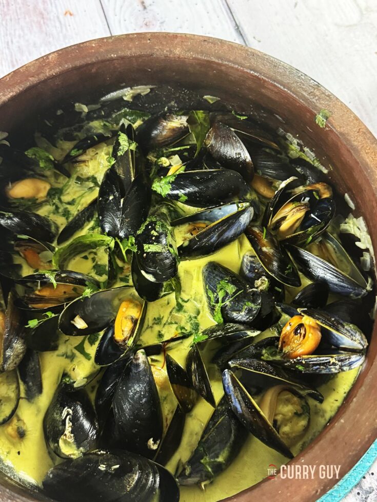 Coconut curry mussels in a clay pot with the curry sauce.