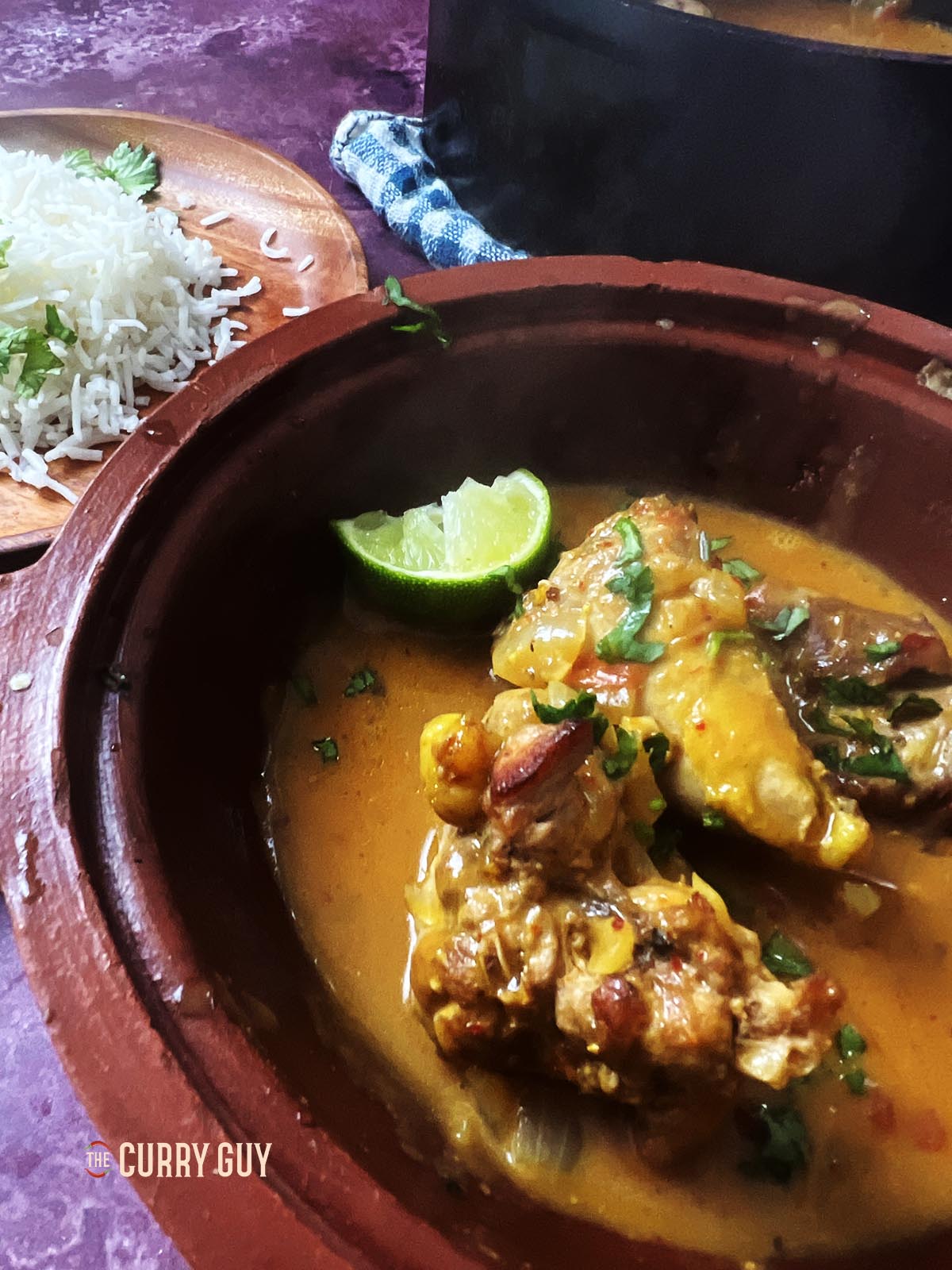 pheasant curry in a serving bowl next to rice at a set table.
