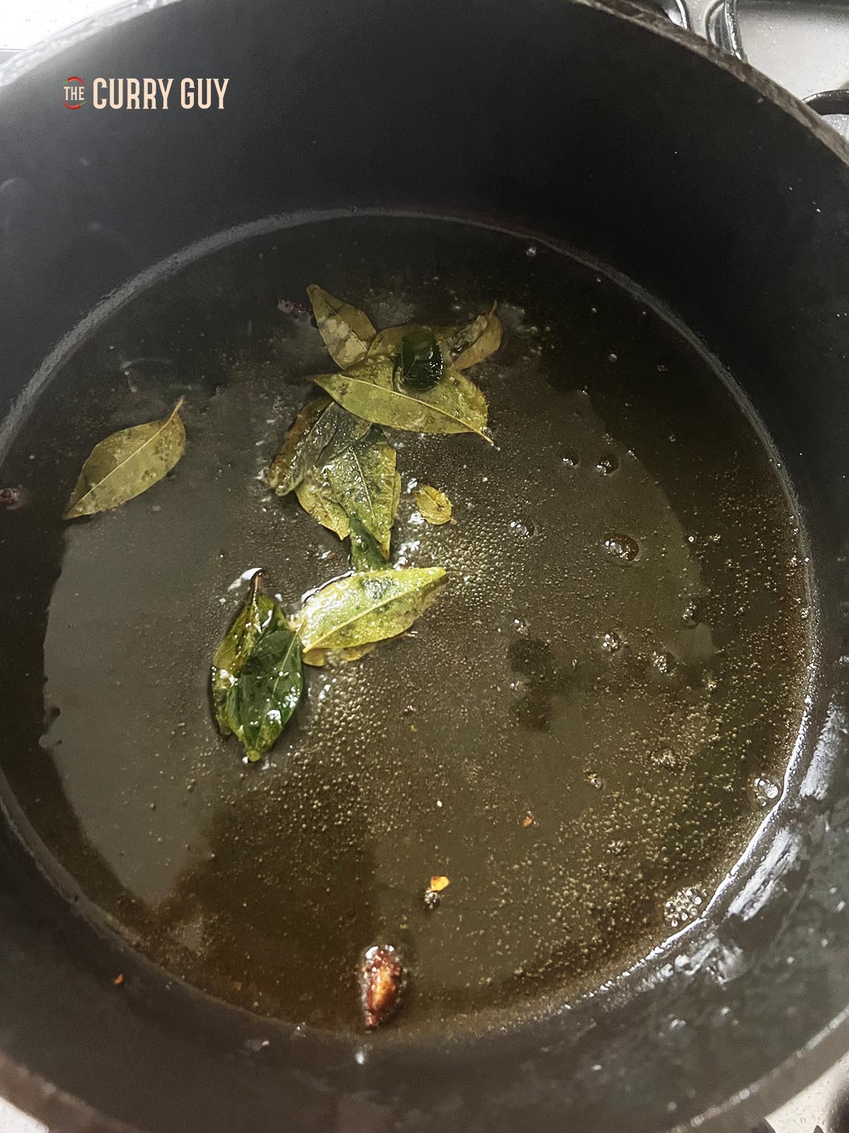 Frying curry leaves in oil to infuse their flavour into the oil. 