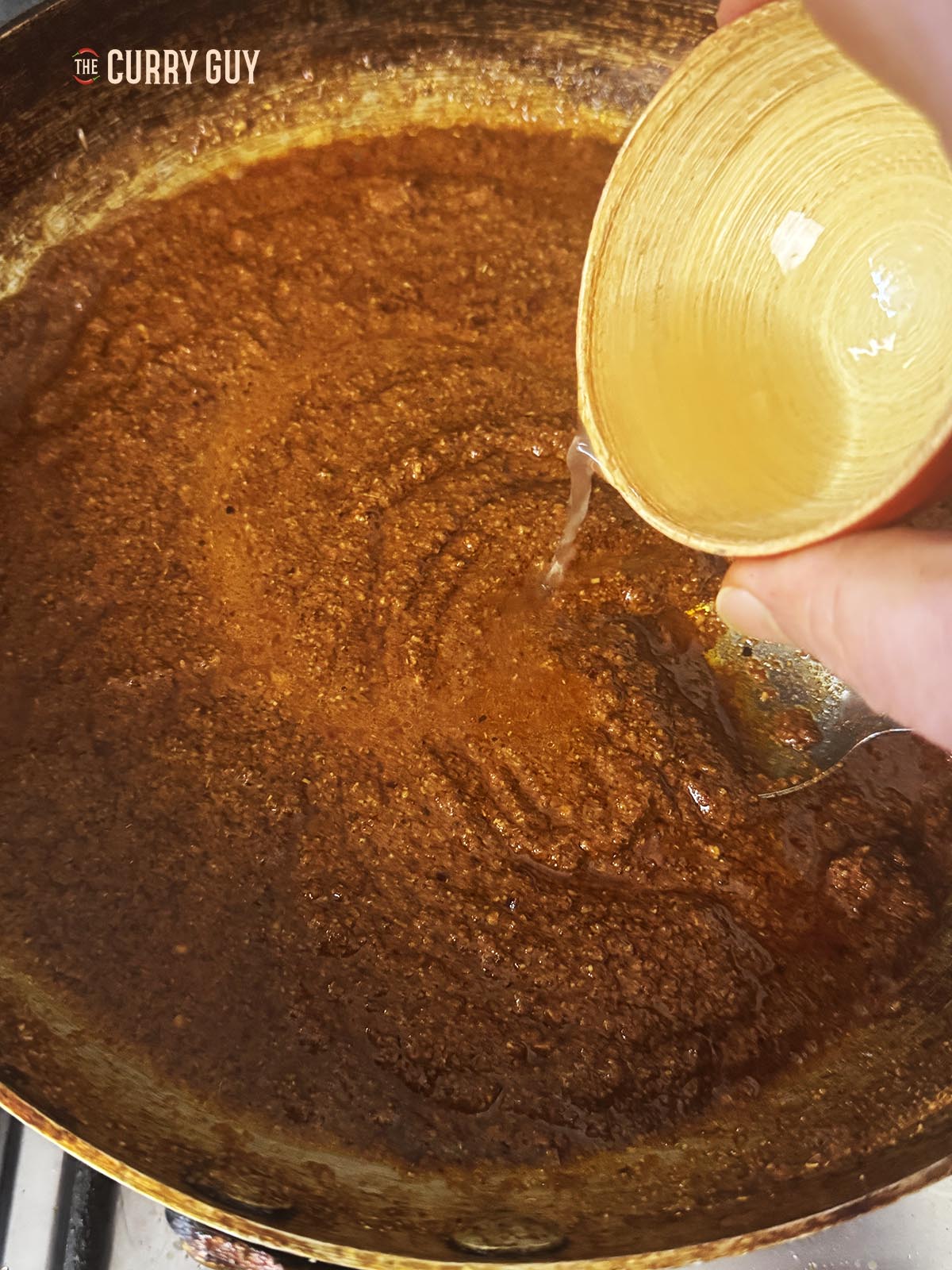 Adding the vinegar to the paste in the pan.