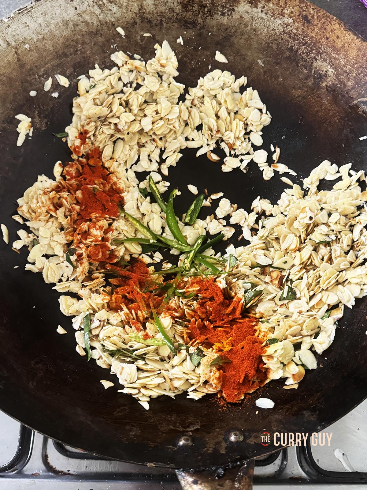 Adding the ground spices, curry leaves and chillies to the almonds.