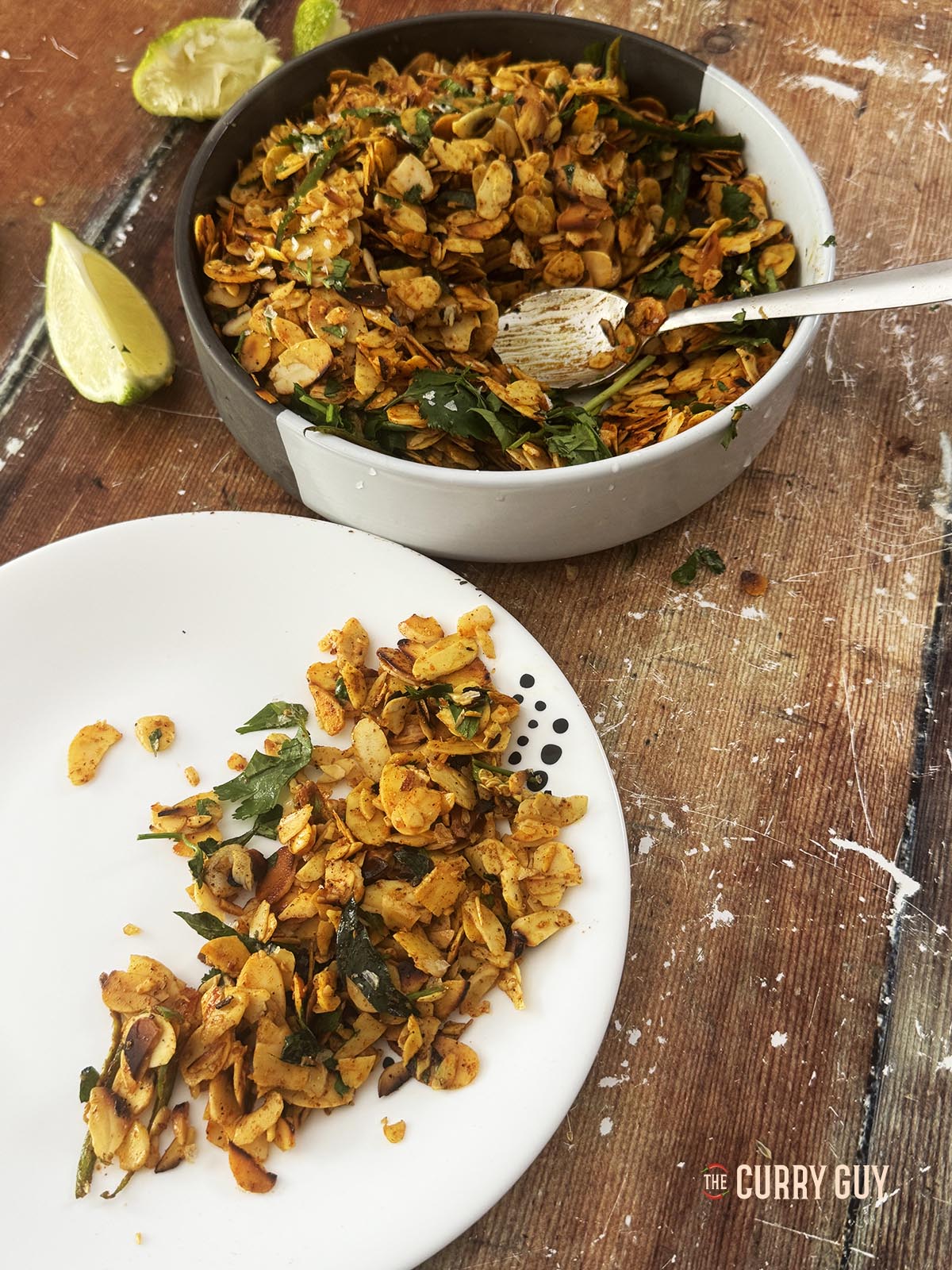 Spiced almonds on a serving plate next to a bowl of all the spicy almonds.