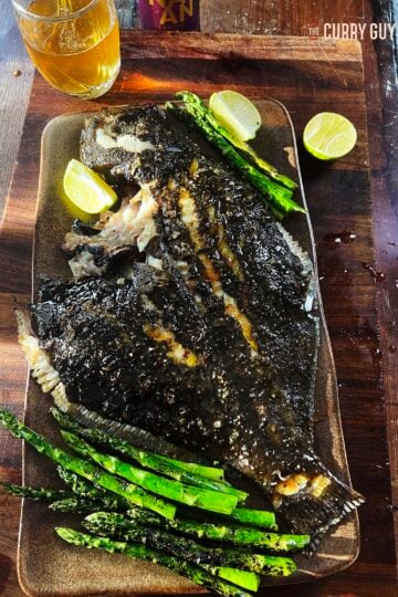 Grilled turbot on a serving platter with vegetables and lime wedges.