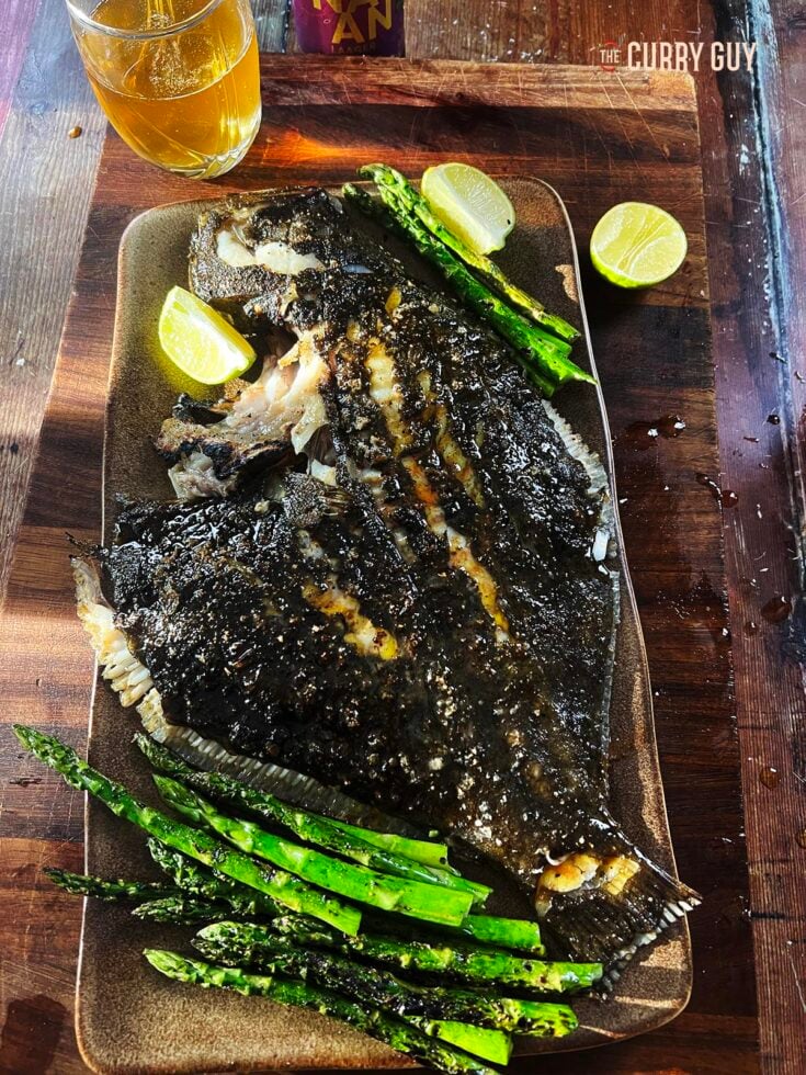 Grilled turbot on a serving platter with vegetables and lime wedges.