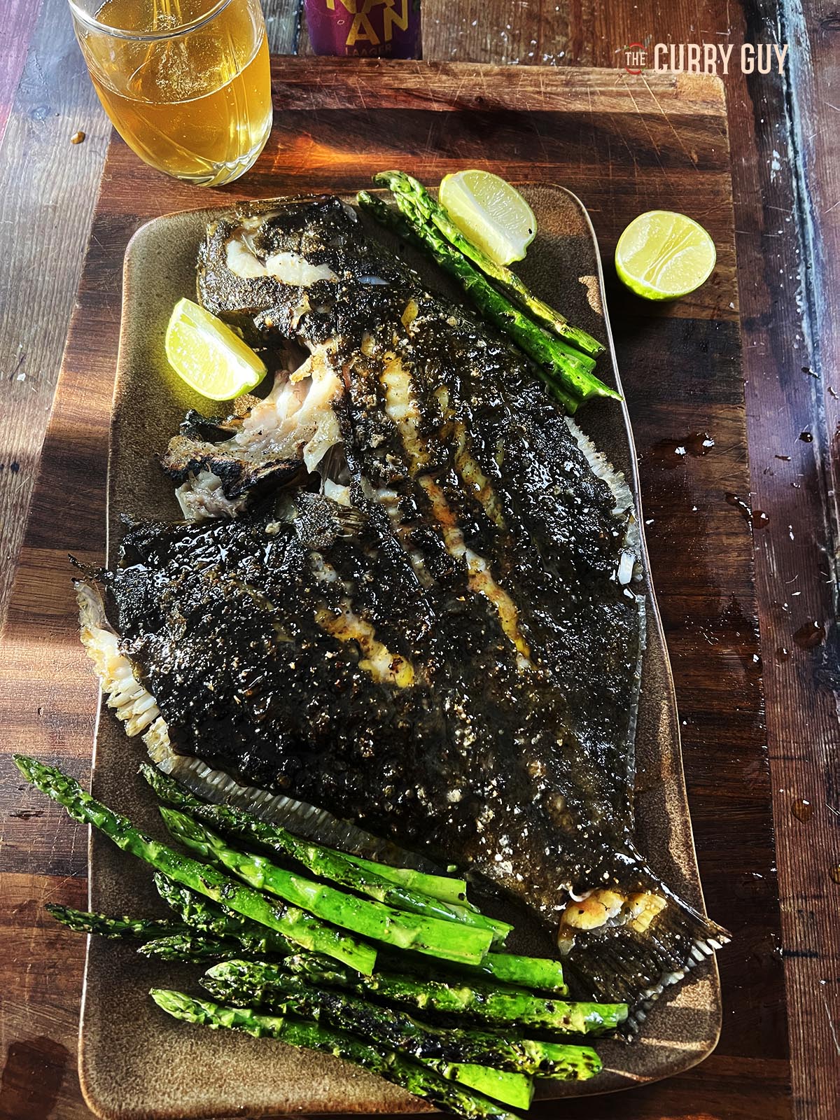 Grilled turbot on a serving platter with vegetables and lime wedges.