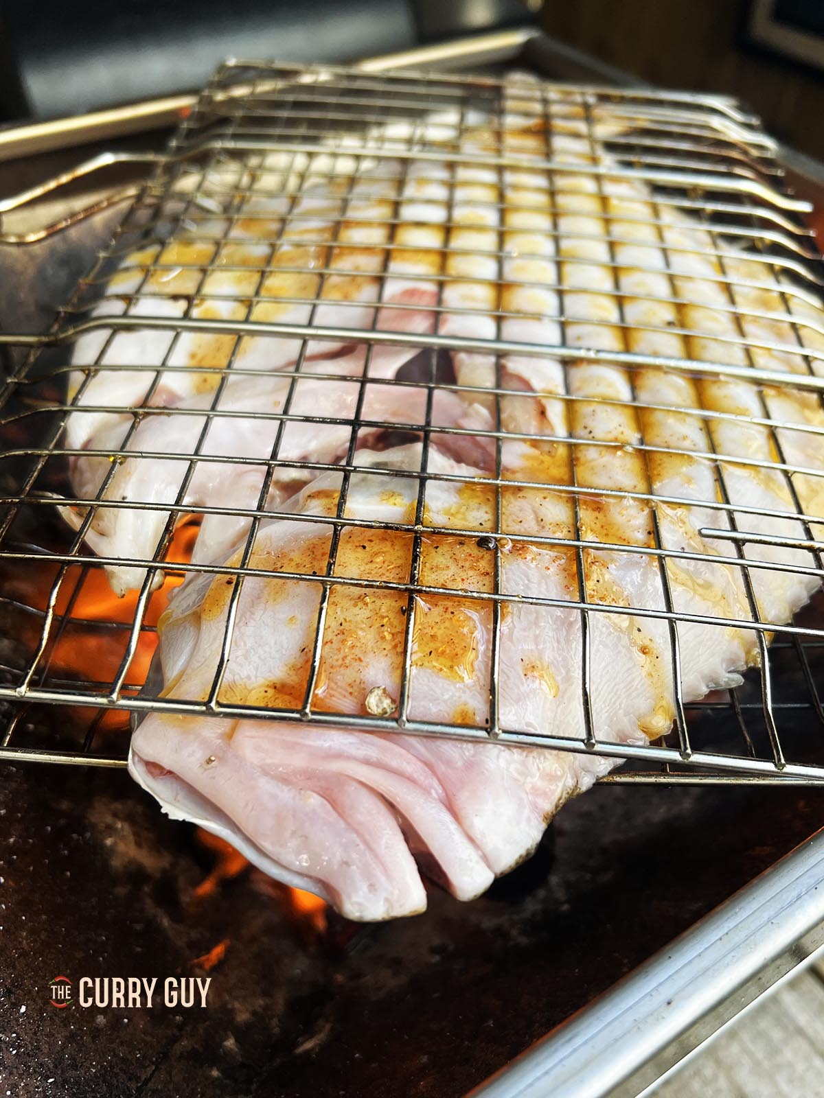 Placing the turbot over the fire in a fish basket.