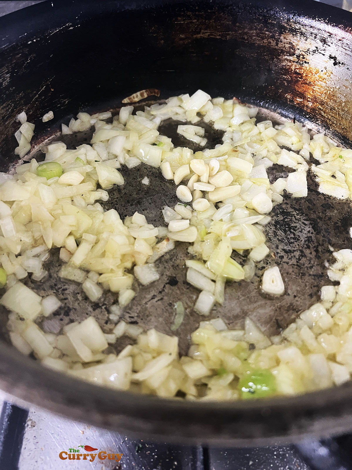 Adding onions and garlic to the frying pan.