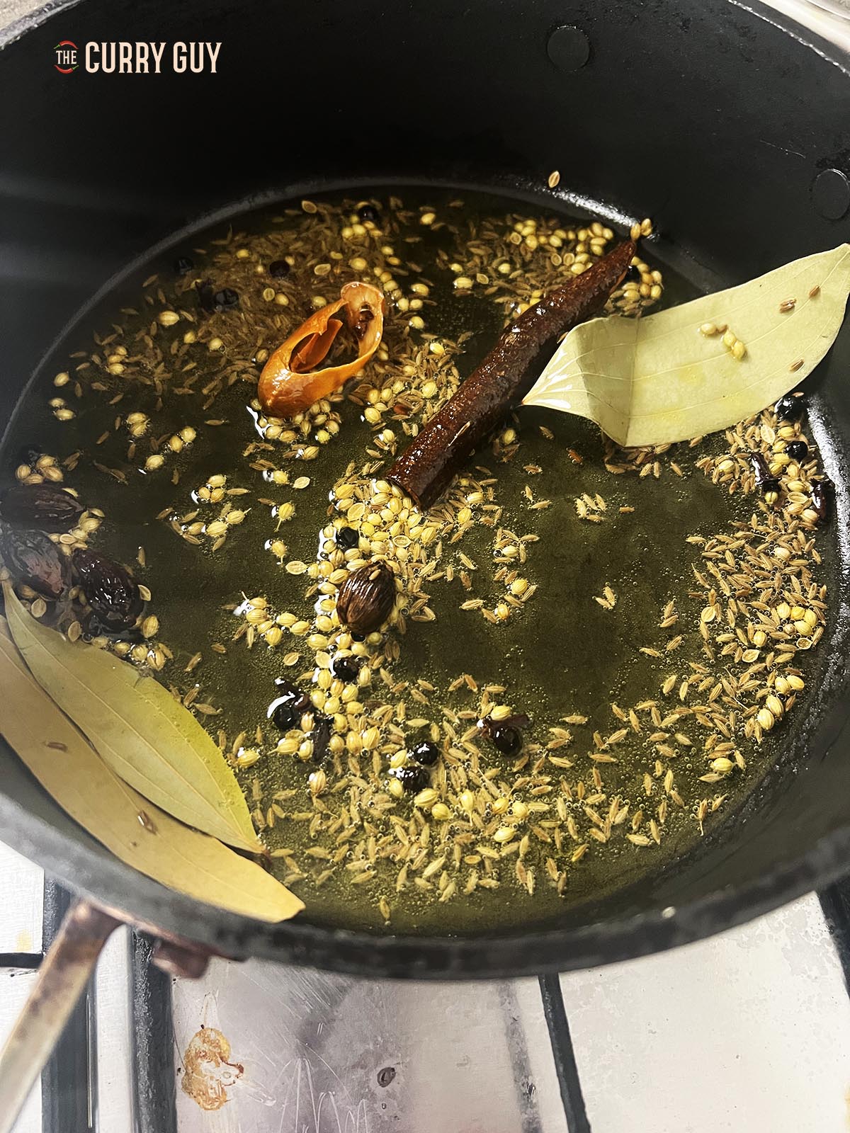 Adding whole spices to infuse into the hot ghee.