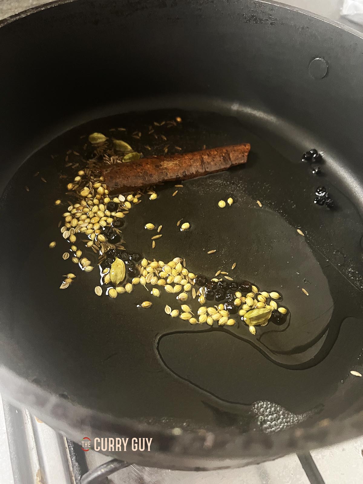 Adding whole spices to oil in a pan to infuse their flavour into the oil. 
