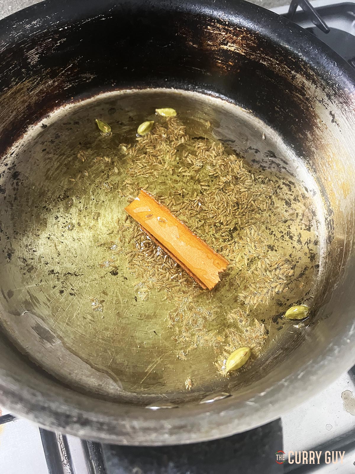 Infusing whole spices into ghee in a frying pan.