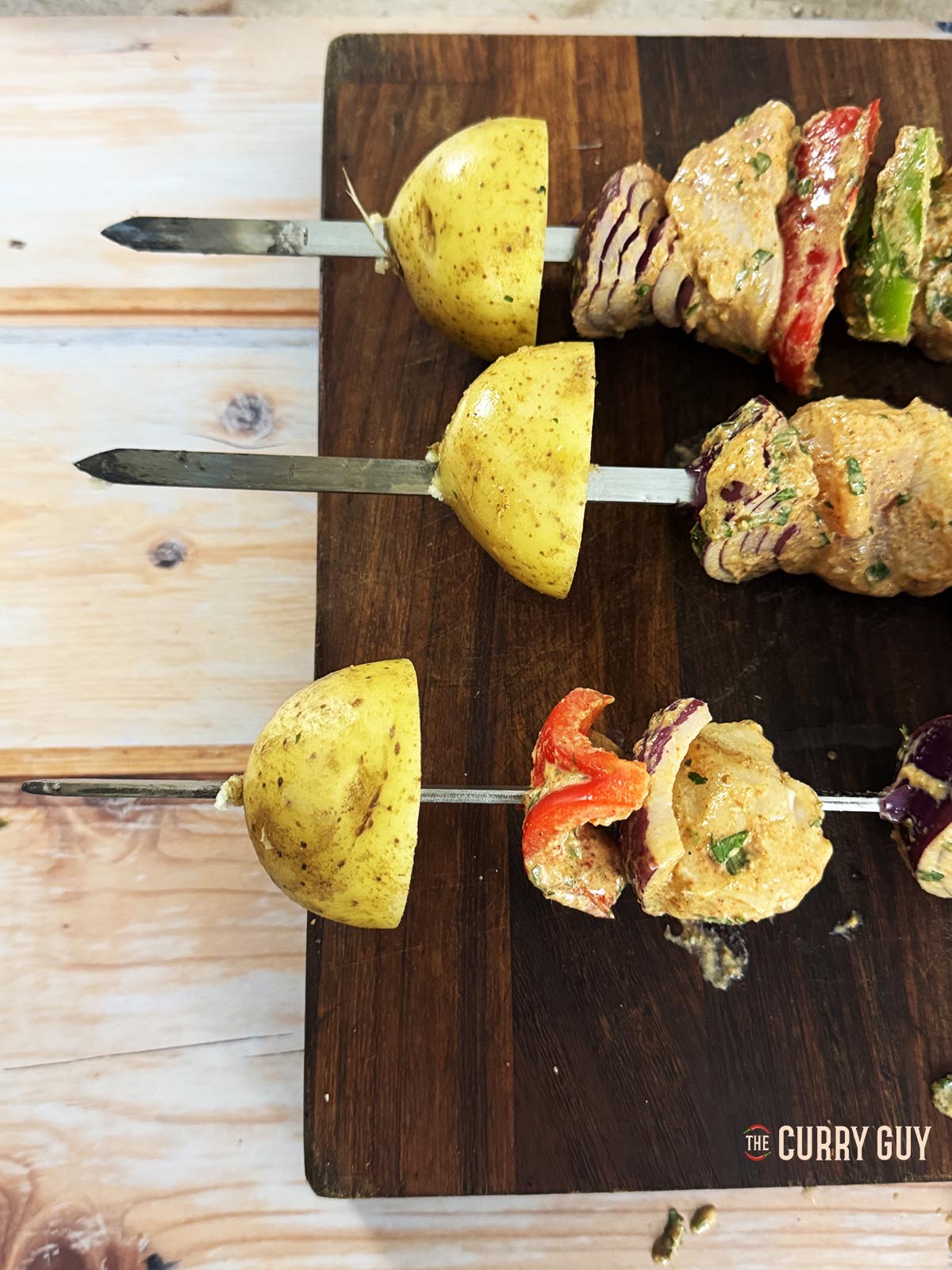 Adding half potatoes onto the ends of skewers for the tandoor.