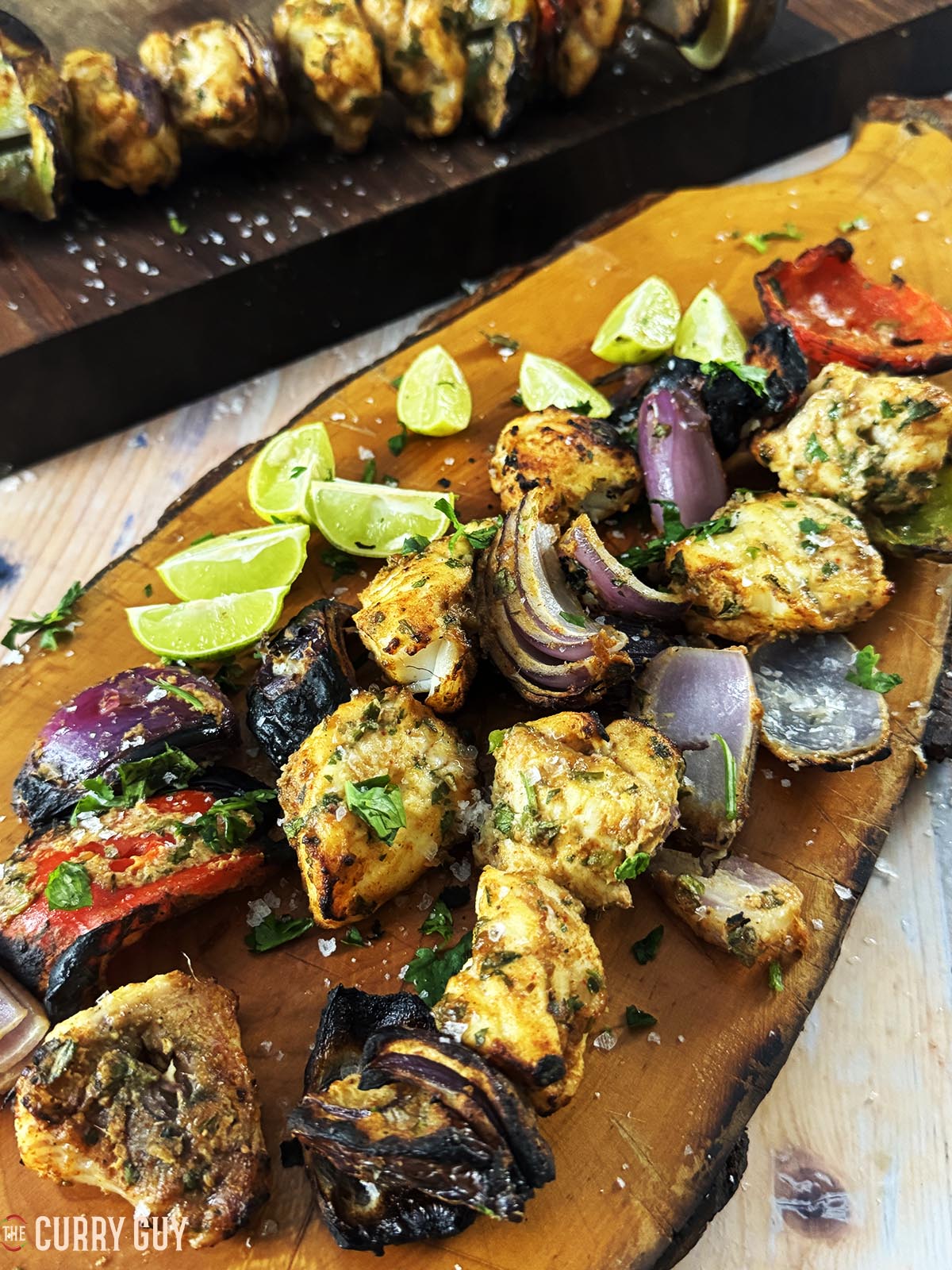 Grilled monkfish on a serving platter with vegetables and lime wedges.