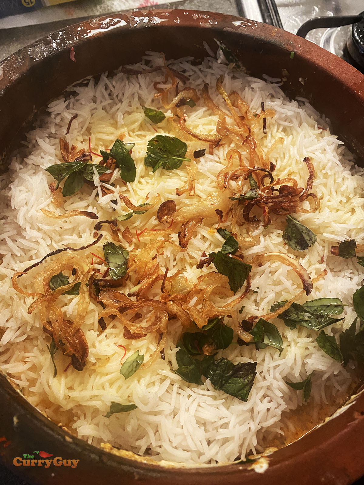 Adding rice, saffron and herbs to the biryani pot.