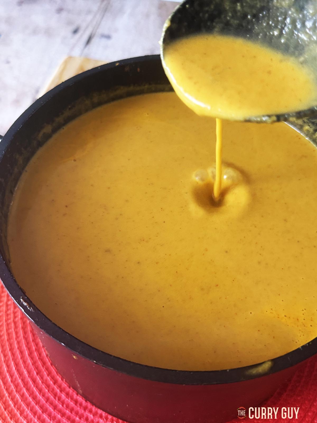 Pouring the base curry sauce from a spoon back into the pot.