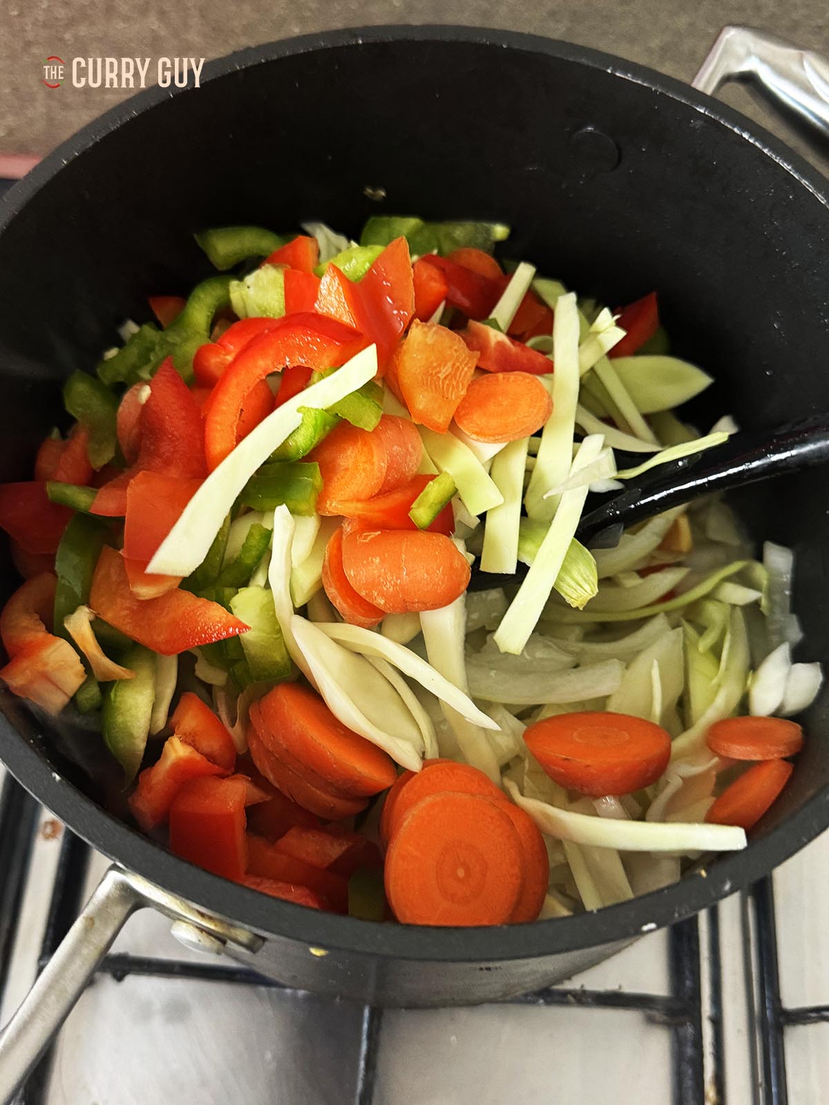 Adding the bell peppers, carrot and cabbage to the pot.