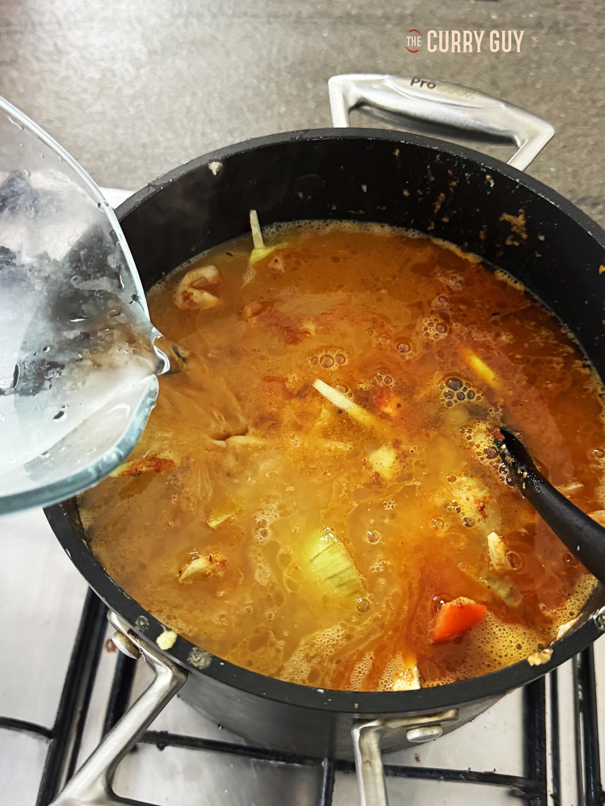 Adding water to the vegetables and spices in the pot.