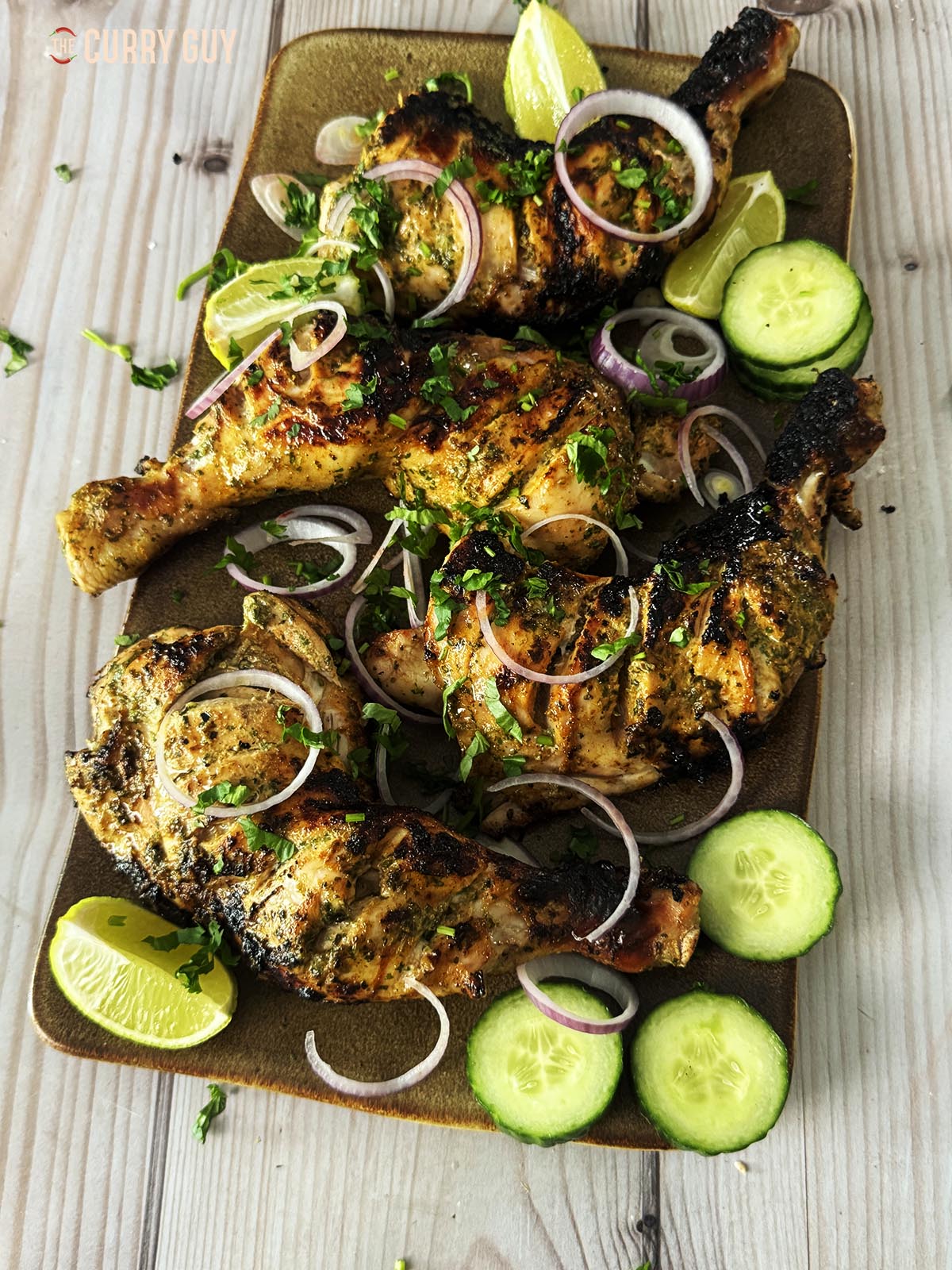 The grilled chicken legs served with lime wedges, sliced red onion and cucumber slices.