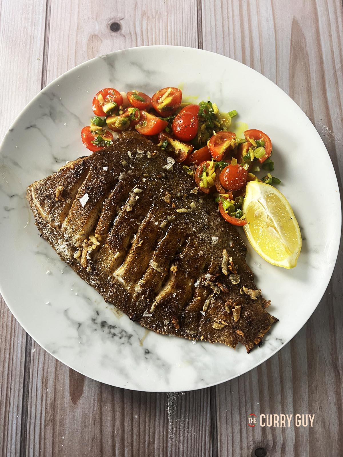 Pan fried lemon sole on a serving plate with garlic butter and turmeric tomatoes.