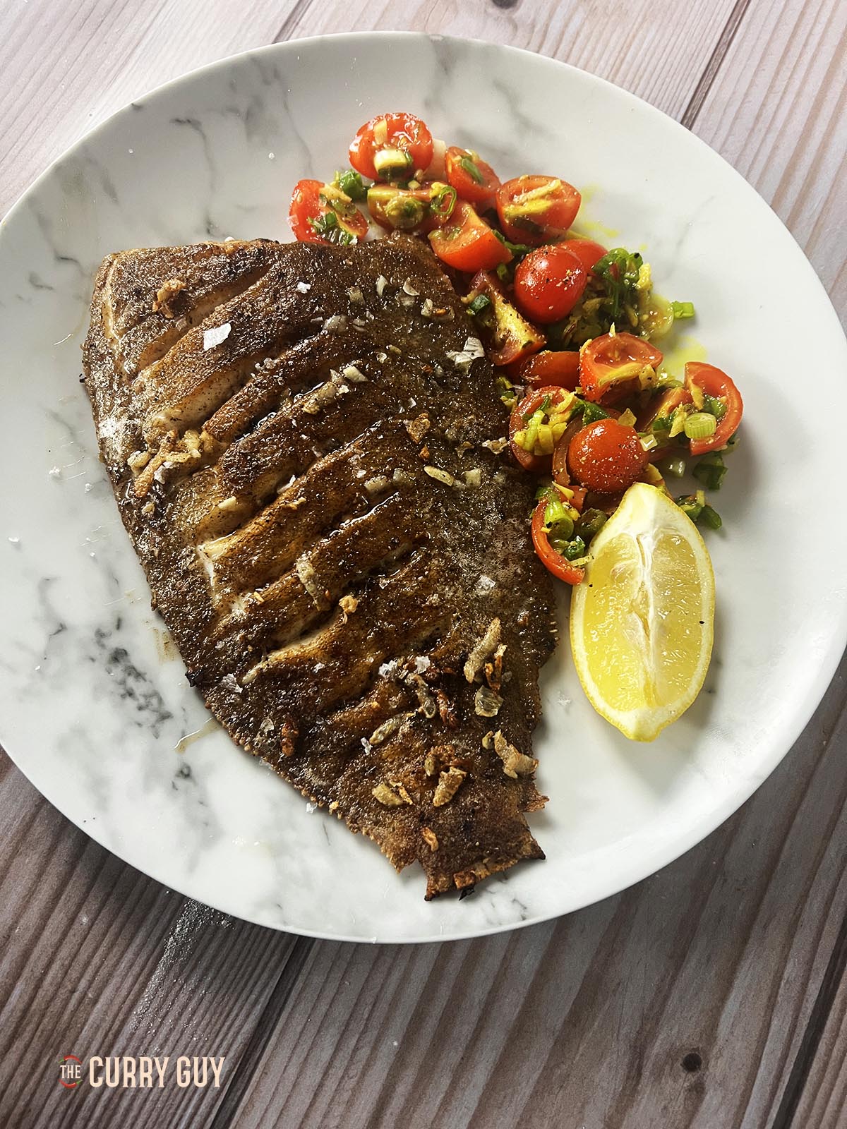 Pan fried lemon sole on a serving plate with turmeric tomatoes.