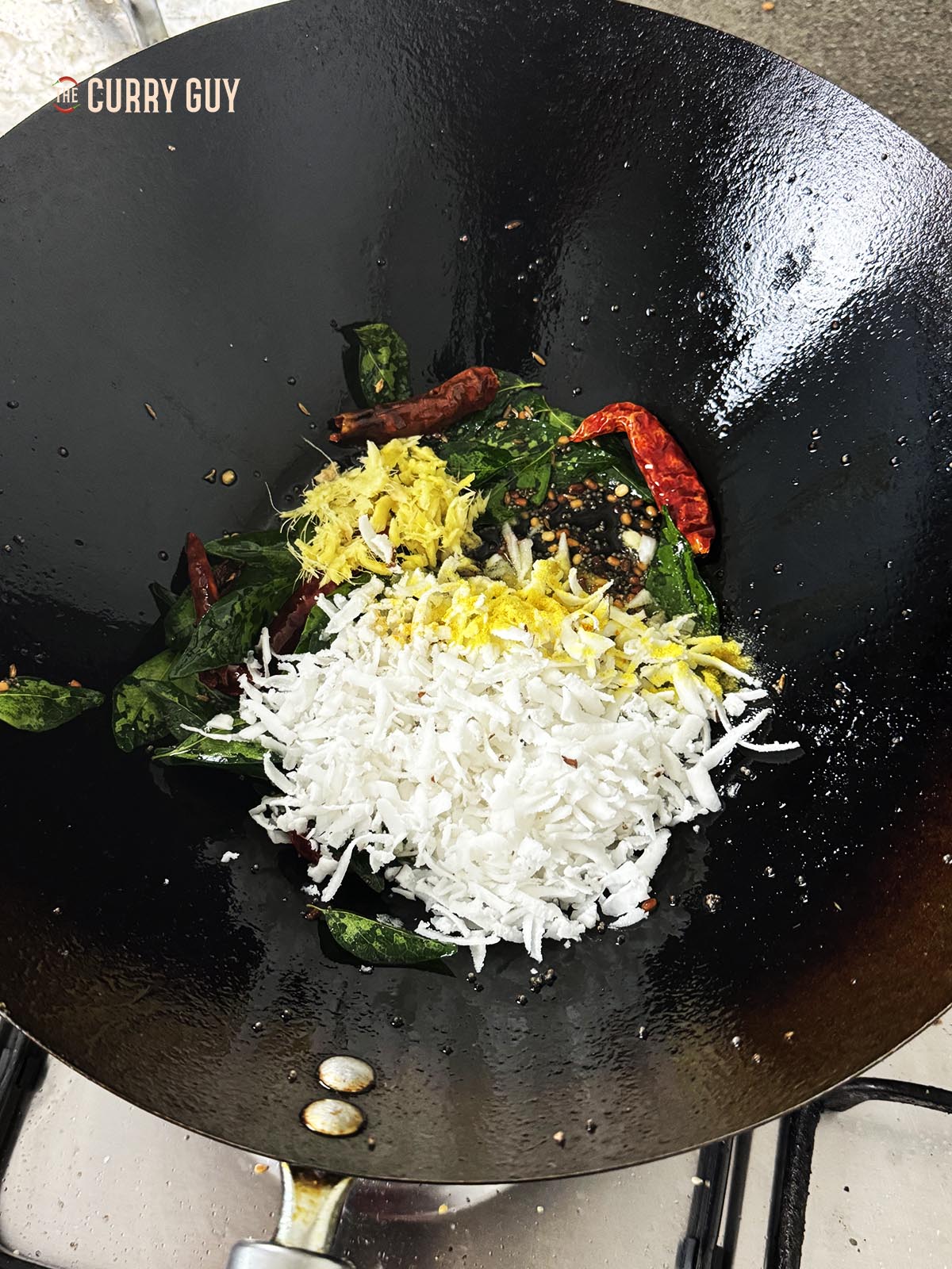 Adding the curry leaves and dry chillies to the pan along with the grated ginger, grated coconut and asafoetida and turmeric.