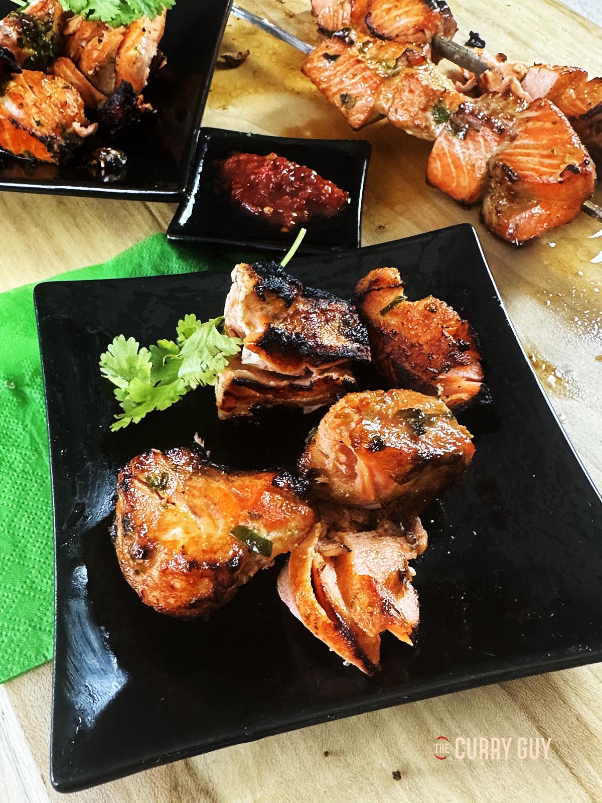 The salmon tikka on a serving plate next to soy sauce and chilli sauce for dipping.