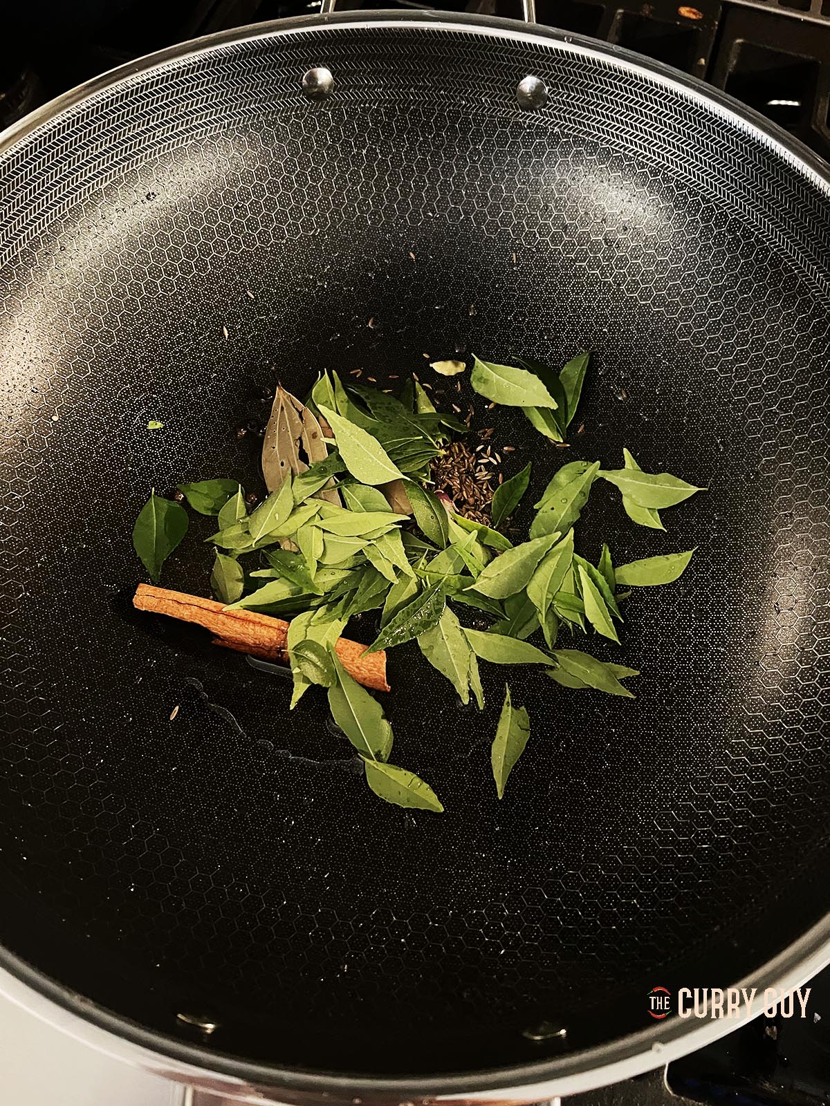 Infusing spices and curry leaves into ghee in the pan.