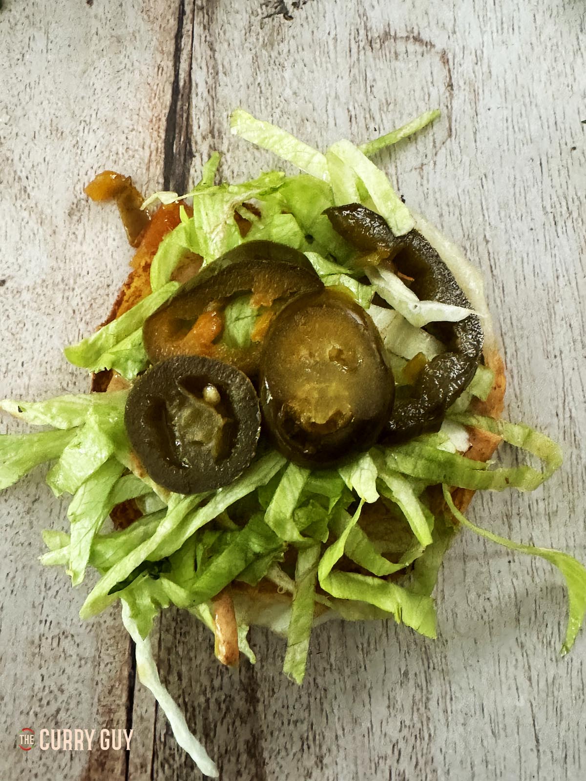 Adding lettuce and pickled chillies to the bottom bun.