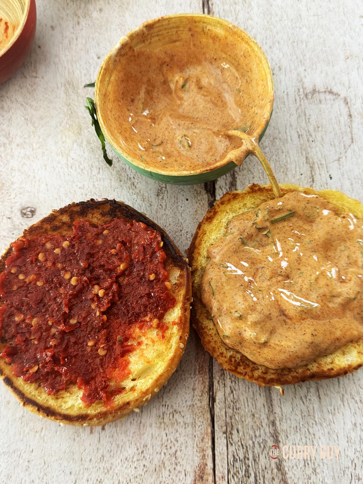 Topping the bottom bun with the burger sauce and the top bun with sambal oelek.