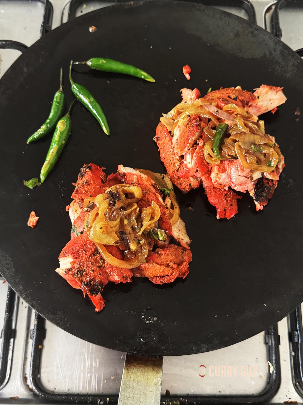 Heating two mounds of shredded chicken on a tawa over medium heat.