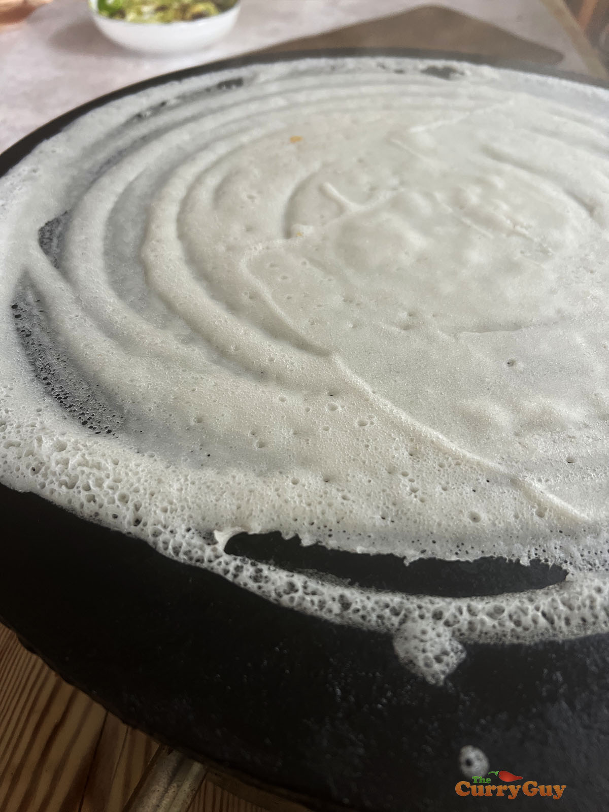 Dosa batter swirled across hot surface.