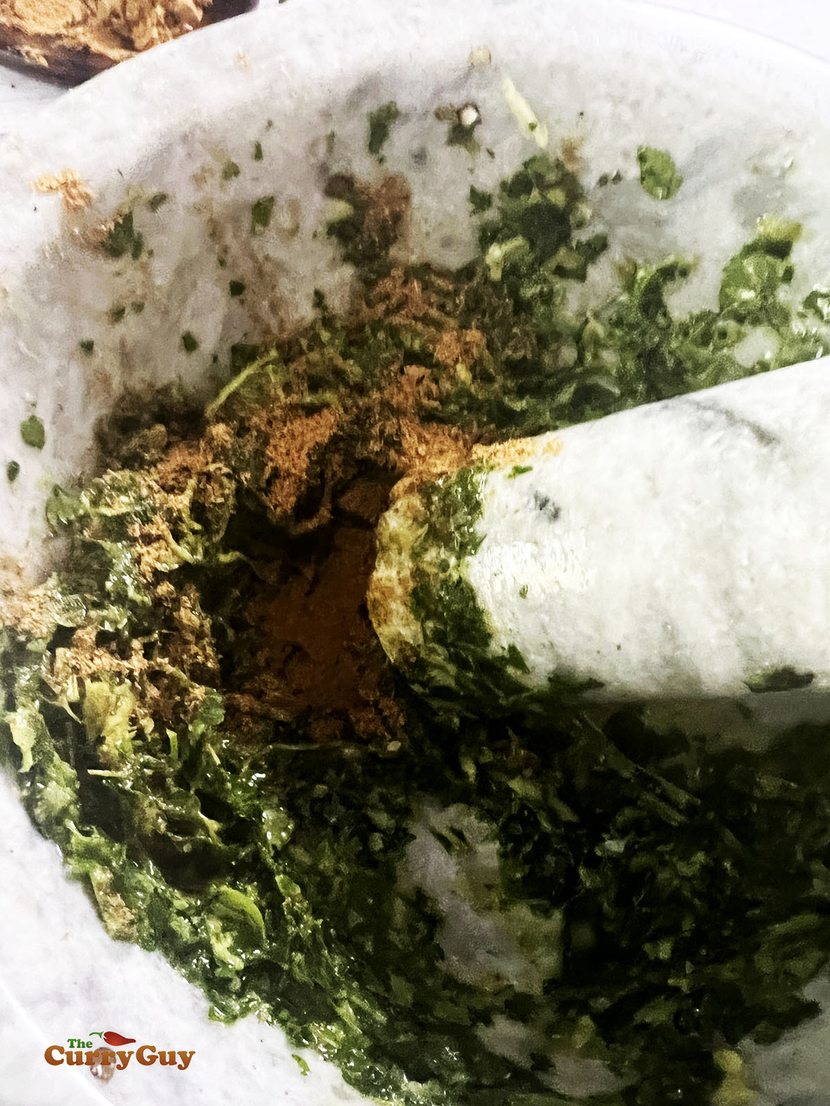 Pounding the green masala ingredients into a paste.