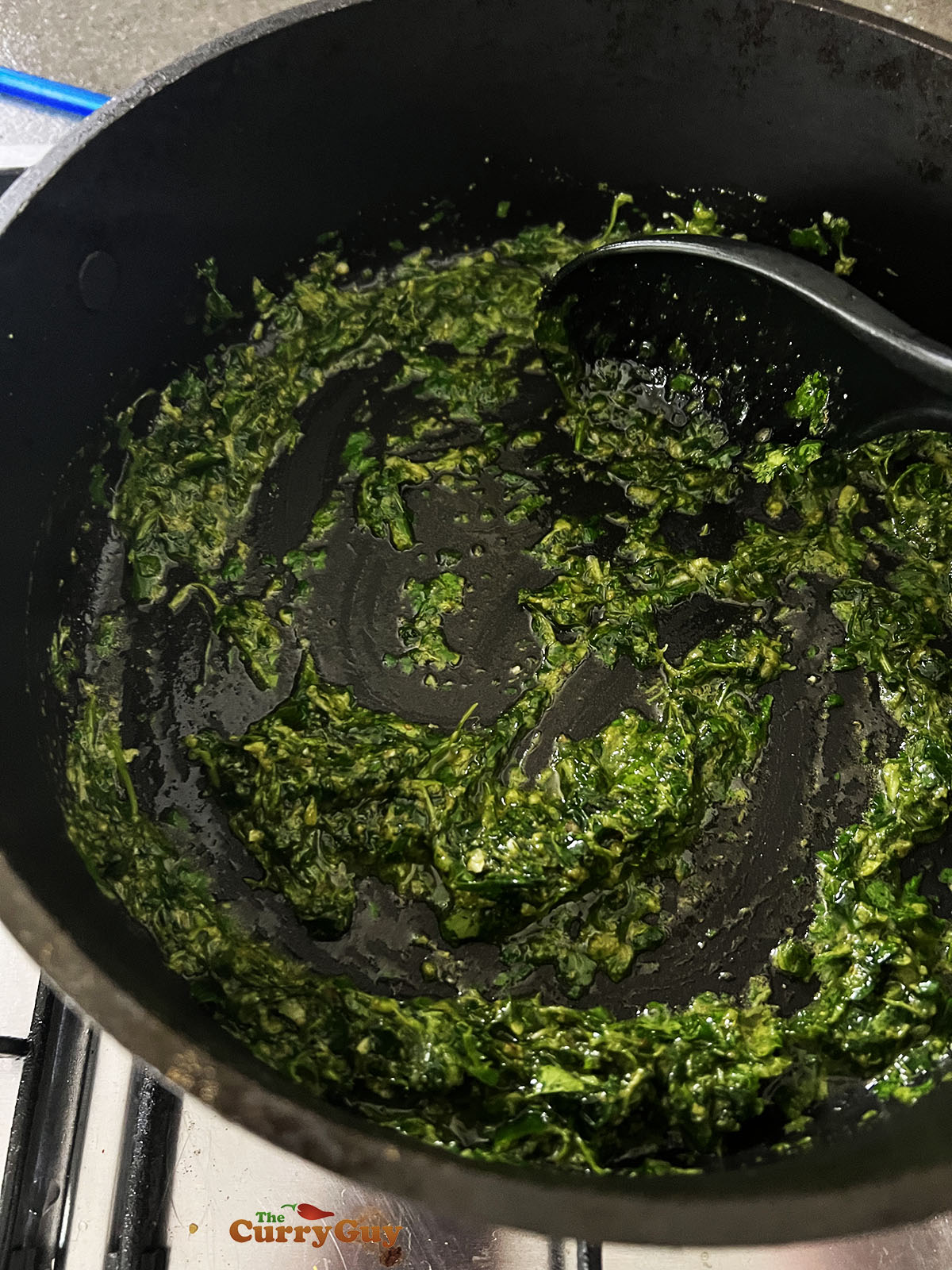 Adding the green paste to the ghee in a pan and frying.