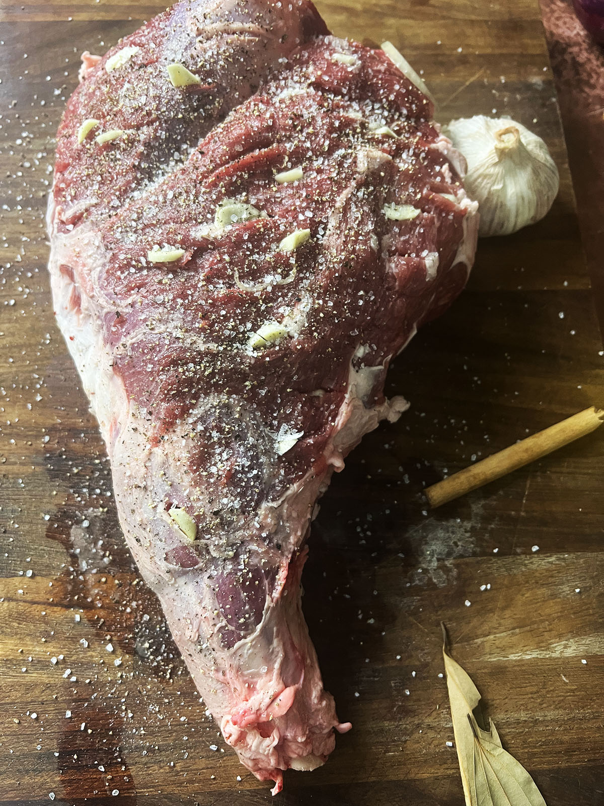 Preparing the lamb raan by removing the fat and filling prepared holes with garlic.