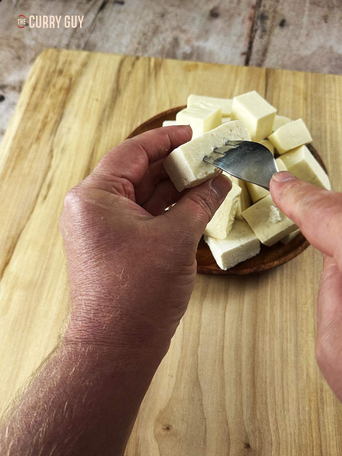 Pricking a piece of paneer with a fork to allow the marinade to soak into it.