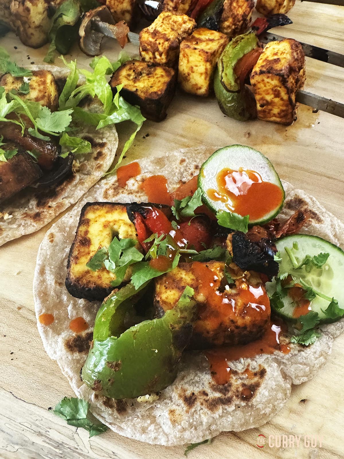 Paneer tikka, roasted vegetables, cold salad vegetable and hot sauce on a chapatti.