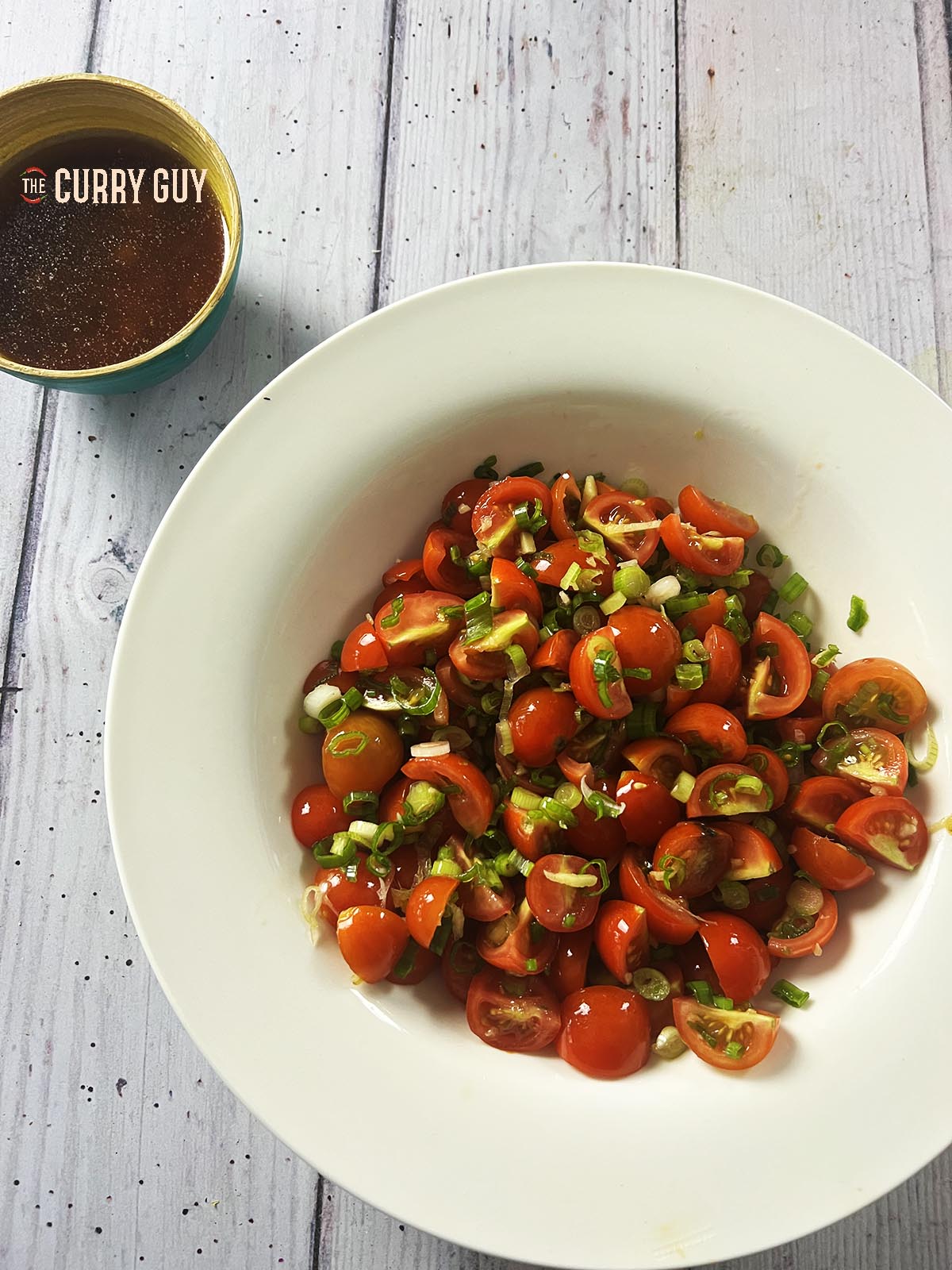 The tomato salad ingredients in a bowl next to the prepared dressing. 