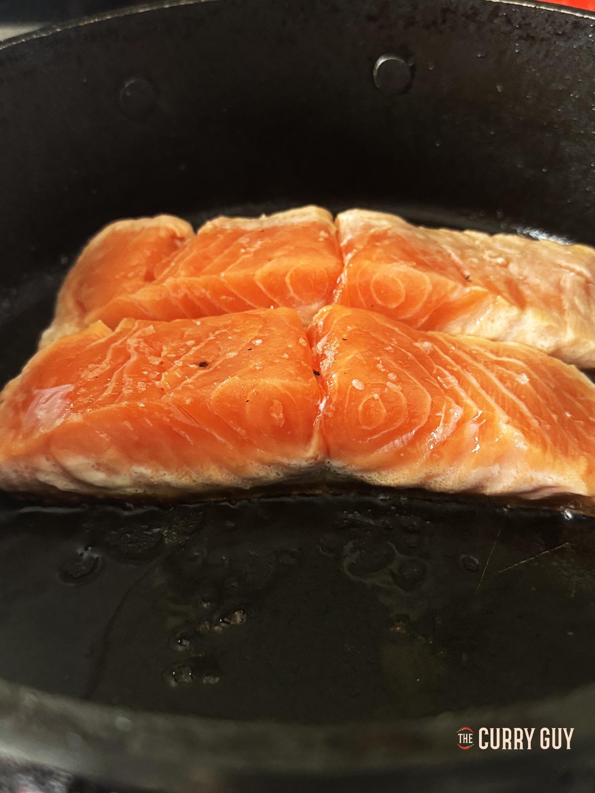The salmon fillets frying, skin side down in the pan.