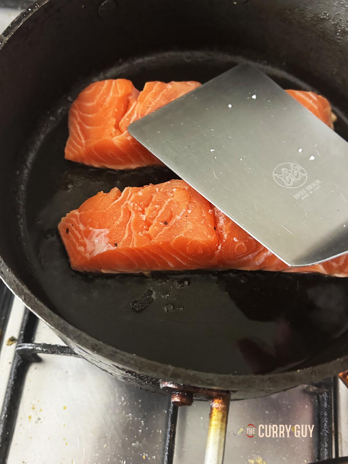 Pressing the salmon fillets down into the pan with a spatula.