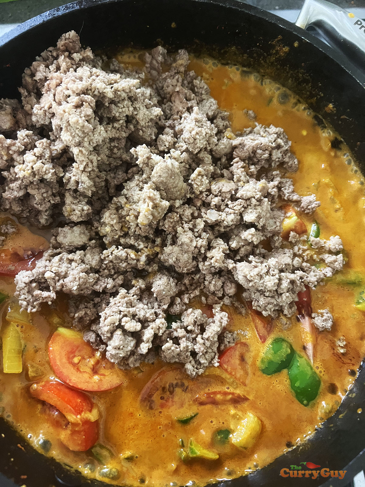 Adding coconut milk, half of the tomatoes and the keema to the curry.