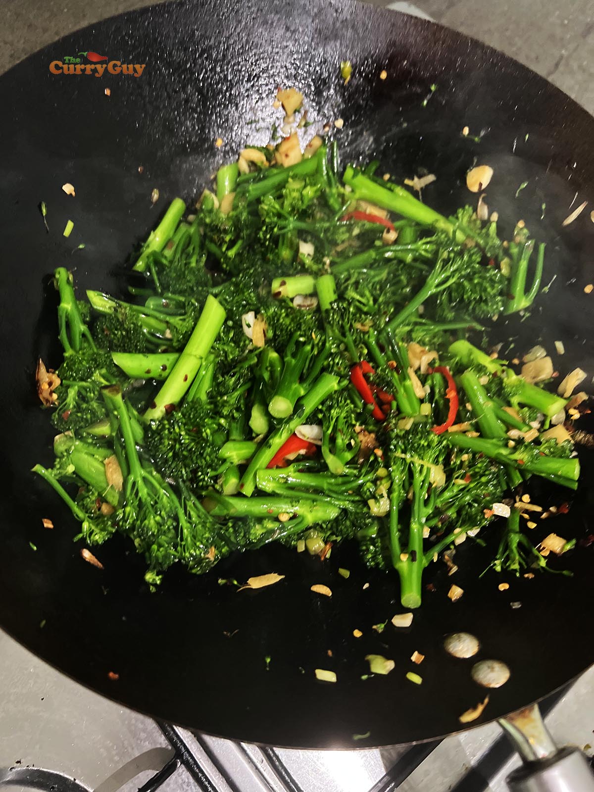 Adding soy sauce to the broccoli in the wok.