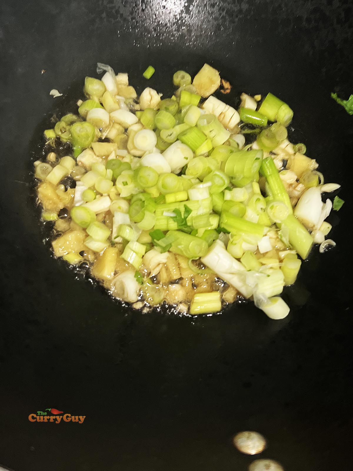 Adding oil, garlic, ginger and spring onions (scallions) to a hot wok.