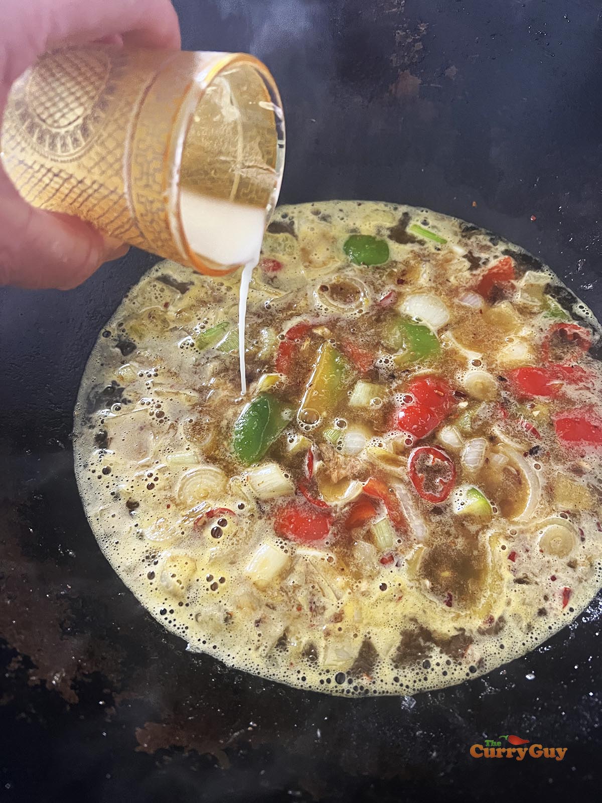 Adding the slurry to the sauce to thicken it. 